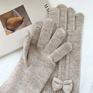 Close-up of beige knit gloves featuring a cute bow detail and thick ribbed cuffs