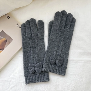 Close-up of dark grey knitted gloves with elegant bow detail on a minimal background
