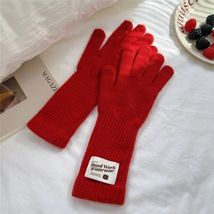 Detail of red knit glove with elongated ribbed cuff and bear embroidered patch label