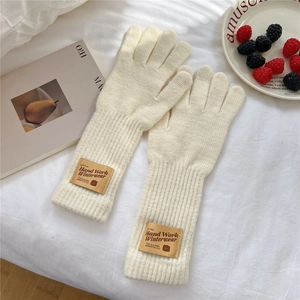 Detail of cream knit gloves with ribbed cuffs and brown leather label on white background