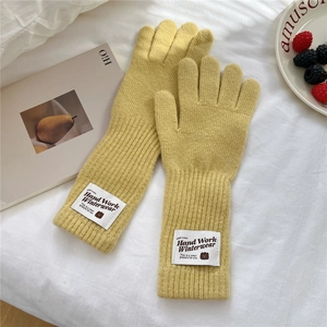 Detailed close-up of yellow knit gloves with warm ribbed texture and handmade brand label