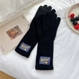 Detail of black knitted gloves featuring a ribbed wrist cuff and decorative bear patch