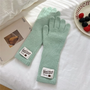 Detail of mint green knitted gloves with bear tag on a cozy lifestyle background