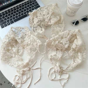 Detailed view of three off-white lace bandanas with floral embroidery and ball fringe