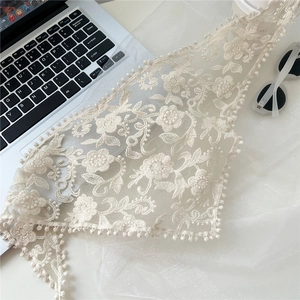 Detail view of cream lace triangle scarf with floral embroidery and ball fringe trim