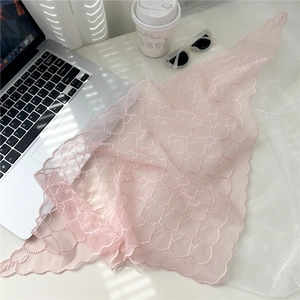 Détail d'un foulard triangle en dentelle rose avec broderie cœur posé sur un bureau moderne