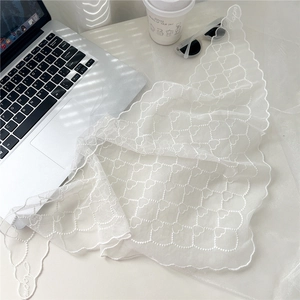 Détail d'un foulard triangulaire en dentelle blanche avec broderie coeur et festons
