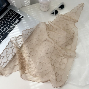 Détail d'une écharpe en dentelle beige avec broderie de cœurs et bord festonné