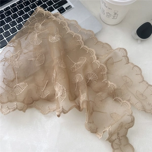 Detail of light brown floral lace scarf draped over lifestyle props with scallop edges