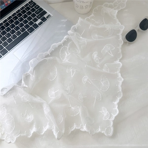Close-up of white lace floral embroidery with ginkgo leaf patterns and wavy edges
