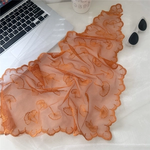 Close-up of orange lace scarf featuring delicate ginkgo leaf embroidery and wavy edges