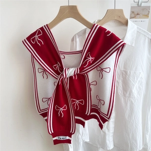 Close-up of knit shawl with red bow patterns, striped edges and brand logo tag