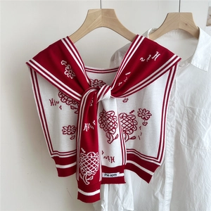 Close-up of knit shawl with red daisy patterns and decorative letter H embroidery