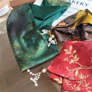Detail of silk-feel scarves with pearl pendants in green, gold, and floral patterns