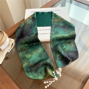 Close-up of dark green silk scarf featuring vintage floral patterns and white pearl tassels