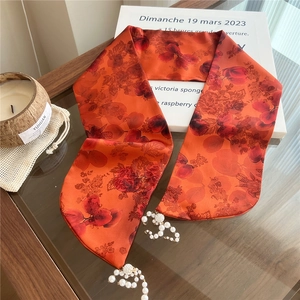 Detail of red floral skinny scarf with pearl and rhinestone charm pendants on a glass table