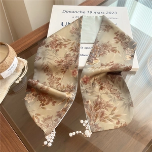 Detail of silk scarf with floral pattern and white pearl tassel charms on wood surface
