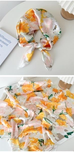 Détail d'un foulard en soie montrant des motifs floraux orange et rose sur du satin