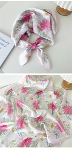 Vue détaillée du motif floral rose et de la texture soyeuse lisse de l'écharpe carrée