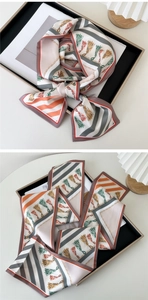 Detailed view of silk-texture scarf featuring tassel and chain prints in a bow knot