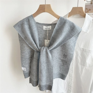 Detail eines grauen Strickschals mit Knotendesign über weißem Hemd an einem Holzbügel