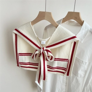Close-up of cream knitted shawl wrap with red stripes and adjustable front bow detail