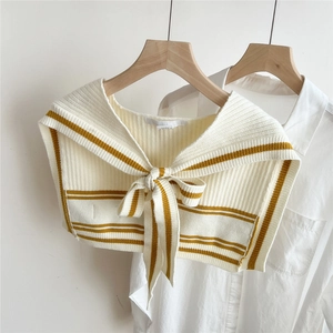Close-up of beige knitted shawl with yellow stripes and elegant bow tie detail