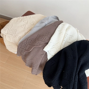 Knitted shawl with heart hollow pattern in five neutral colors stacked on a stool
