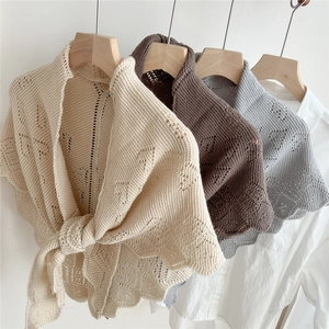 Close-up of hollowed knit shawls in beige and brown with elegant wavy edges and front ties