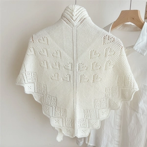 Detail of white knit triangle shawl featuring heart hollow patterns on a wooden hanger