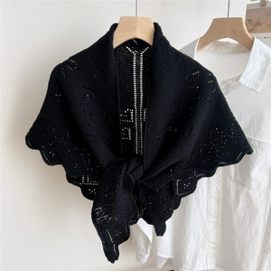 Detail of hand-crocheted black knit shawl tied over white shirt on a wooden hanger