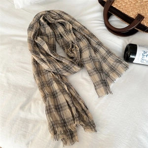 Detail of beige and black plaid cotton linen scarf with frayed edges on a white fabric