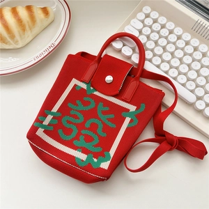 Red knit crossbody phone bag with green graphic design on a white desktop with a keyboard
