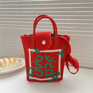 Detail of red knitted crossbody bag with green geometric pattern and metal clasp button