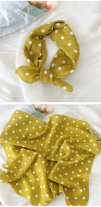 Détail d'un bandana en lin de coton jaune à pois noué en nœud sur un fond en tissu blanc