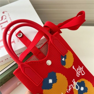 Détail du sac tricoté rouge avec poignée silicone, bouton pression et broderie Joy