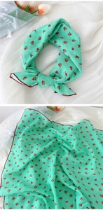 Détail d'un foulard vert menthe avec ourlet rouge et motif floral délicat sur tissu léger