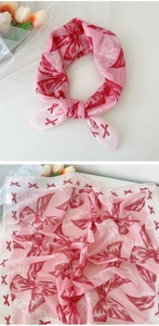 Gros plan d'un foulard en soie rose léger avec imprimé nœuds rouges et décor floral