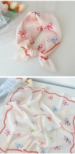 Détail d'un foulard en lin avec motifs de nœuds et bords cousus ondulés rouges sur tissu écru
