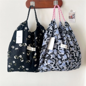 Floral drawstring canvas tote bags in black and blue hanging on a minimalist wall
