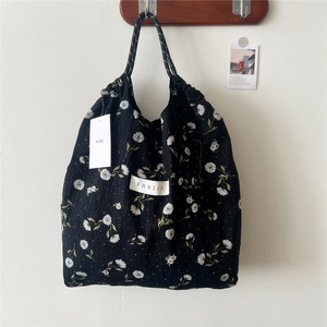 Detail of floral drawstring tote bag with woven handles and brand label on white wall