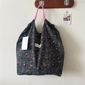 Close-up of floral tote bag with pink rope handles and brand label on white wall