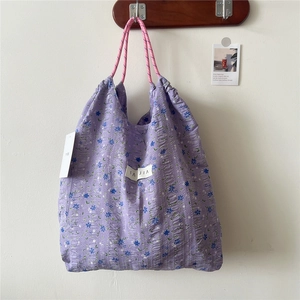 Detail of purple floral tote bag with drawstring texture and woven pink handle