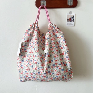Detailed view of floral drawstring tote with pink rope handles and brand label on canvas