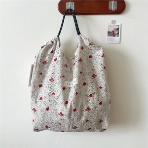 Detailed view of floral canvas tote bag featuring woven rope handles and red flower patterns