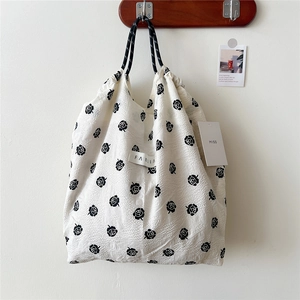 Close-up of floral tote bag with black rose prints, drawstring closure and woven handle