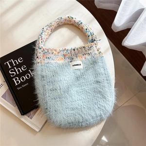 Close-up of light blue plush knitted tote bag with colorful handles and woven label