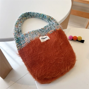 Detail view of plush orange tote bag featuring blue braided handles and Stannum label