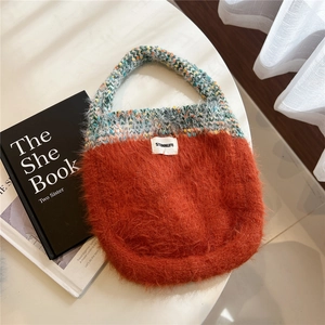 Detail of orange faux fur knit handbag with rainbow handles and brand label on a desk