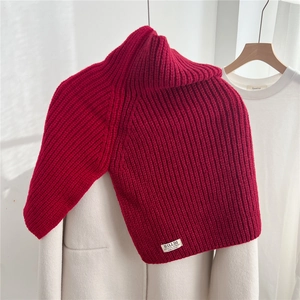 Detailed view of red chunky knit turtleneck shawl with designer patch on white coat